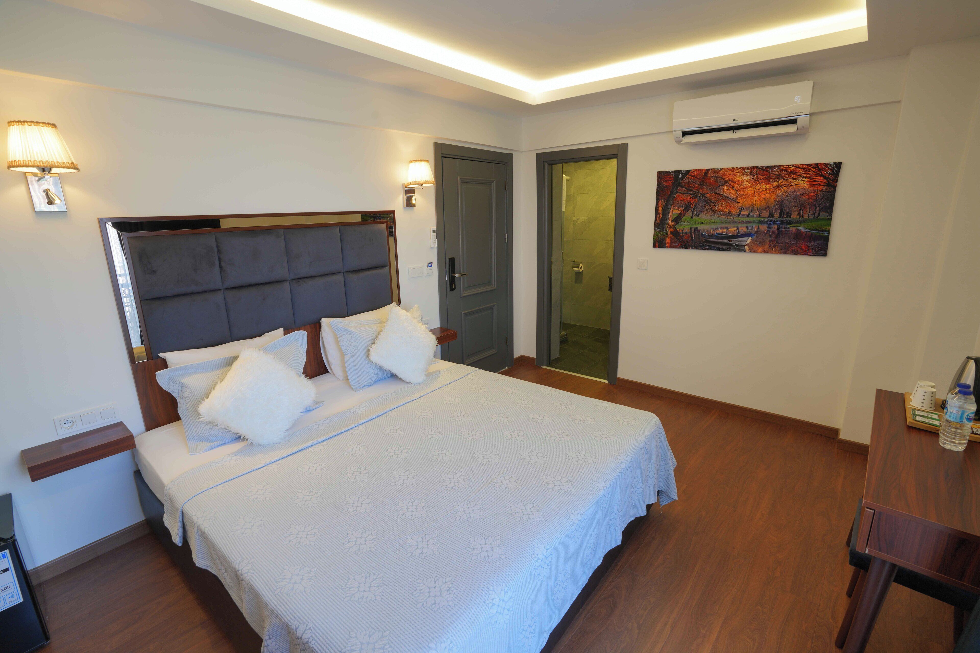 Un dormitorio con cama, mesitas de noche, un equipo de aire acondicionado y un cuadro en la pared.