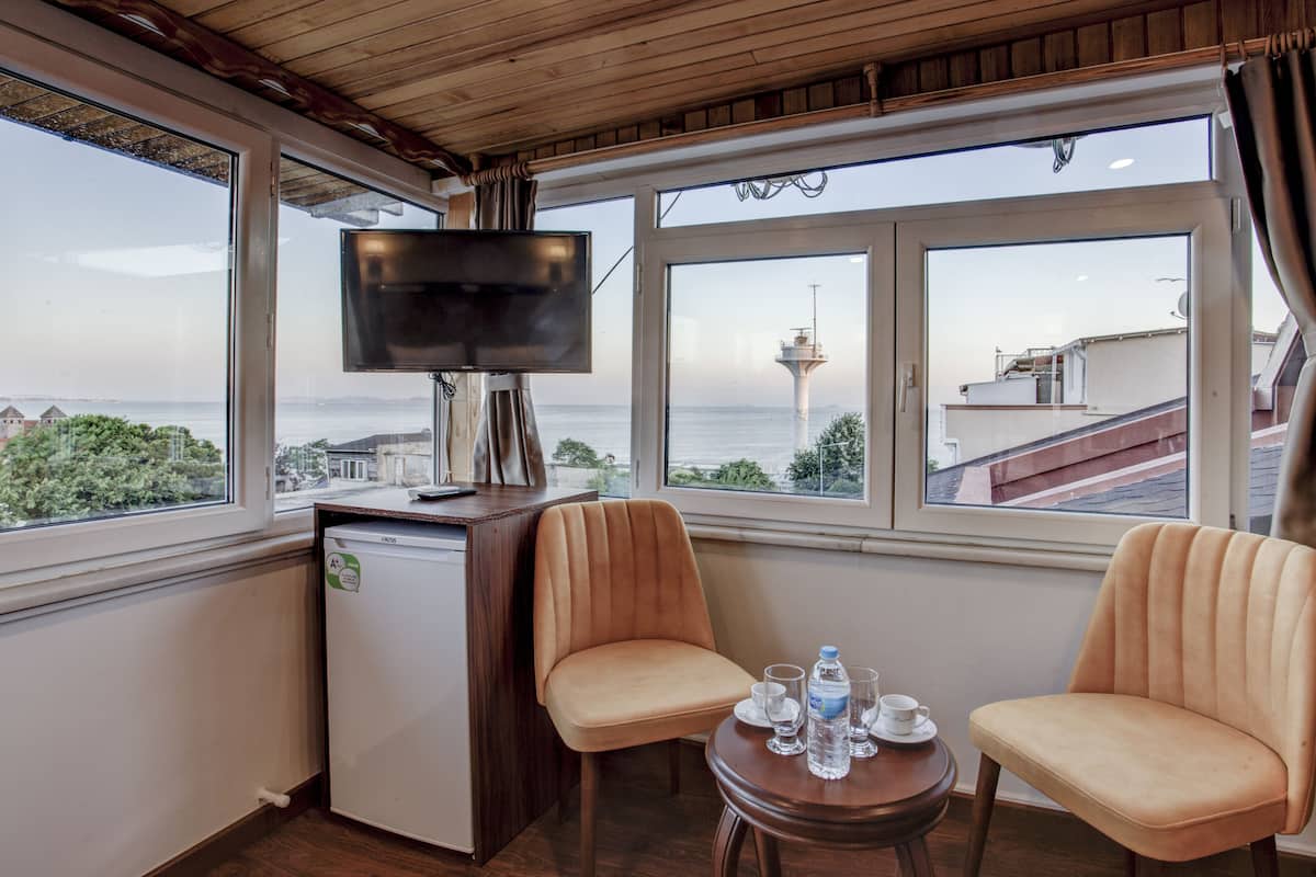 A compact room with a TV, two chairs, a small table, and a view of the sea and a tower.