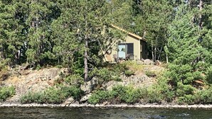 Une petite cabane entourée d’une forêt dense, avec une côte rocheuse en premier plan.