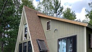 Une cabane dotée d’un toit en pente, de grandes fenêtres et d’une terrasse avec des chaises.