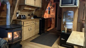 Un intérieur de chalet chaleureux avec un poêle à bois, un coin cuisine et un distributeur d’eau.