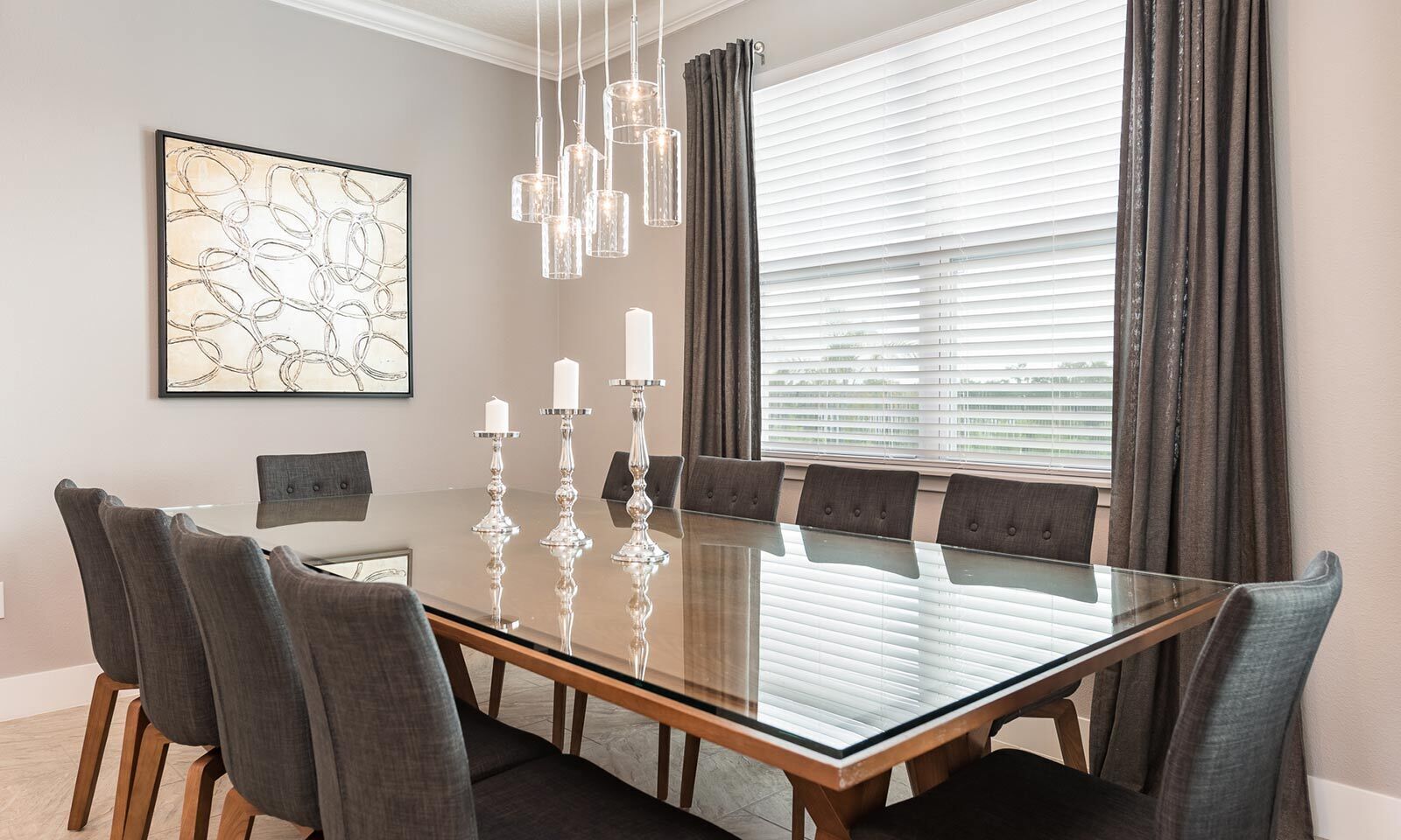 Uma sala de jantar moderna com mesa de vidro, seis cadeiras, um lustre e uma janela grande com cortinas.