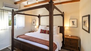 Een hemelbed met houten hoofdbord, wit beddengoed en een rode deken. Twee nachtkastjes met lampen en ingelijste foto’s aan de muur.