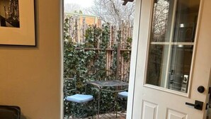Een kamer met een donker houten vloer, een witte deur met een ruit en een kleine tafel met blauwe stoelen.