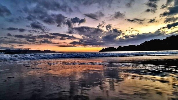 A beach with waves at sunset. - New modern compact home, warm & cosy, Blue Bay beach bach! (Mahia)