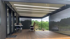 An outdoor deck with a covered area, a table, chairs, and a bench. - New modern compact home, warm & cosy, Blue Bay beach bach! (Mahia)