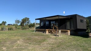 A modern, single-story house with a covered porch and a satellite dish. - New modern compact home, warm & cosy, Blue Bay beach bach! (Mahia)
