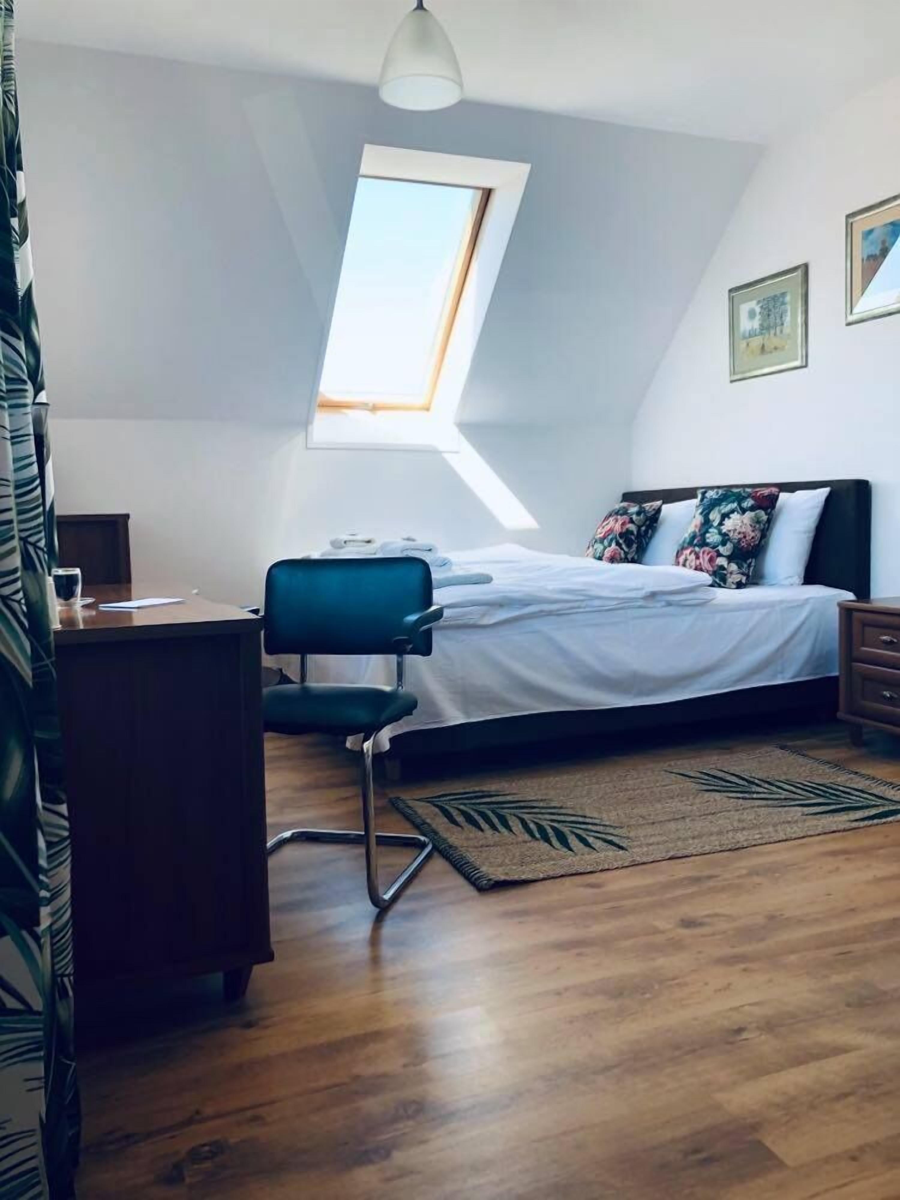 Un dormitorio con tragaluz, una cama con almohadones estampados, un escritorio y una silla.