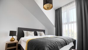 A modern bedroom with a large bed, a bedside table, a lamp, and a window with curtains. - Coffee Inn (Kolbudy)