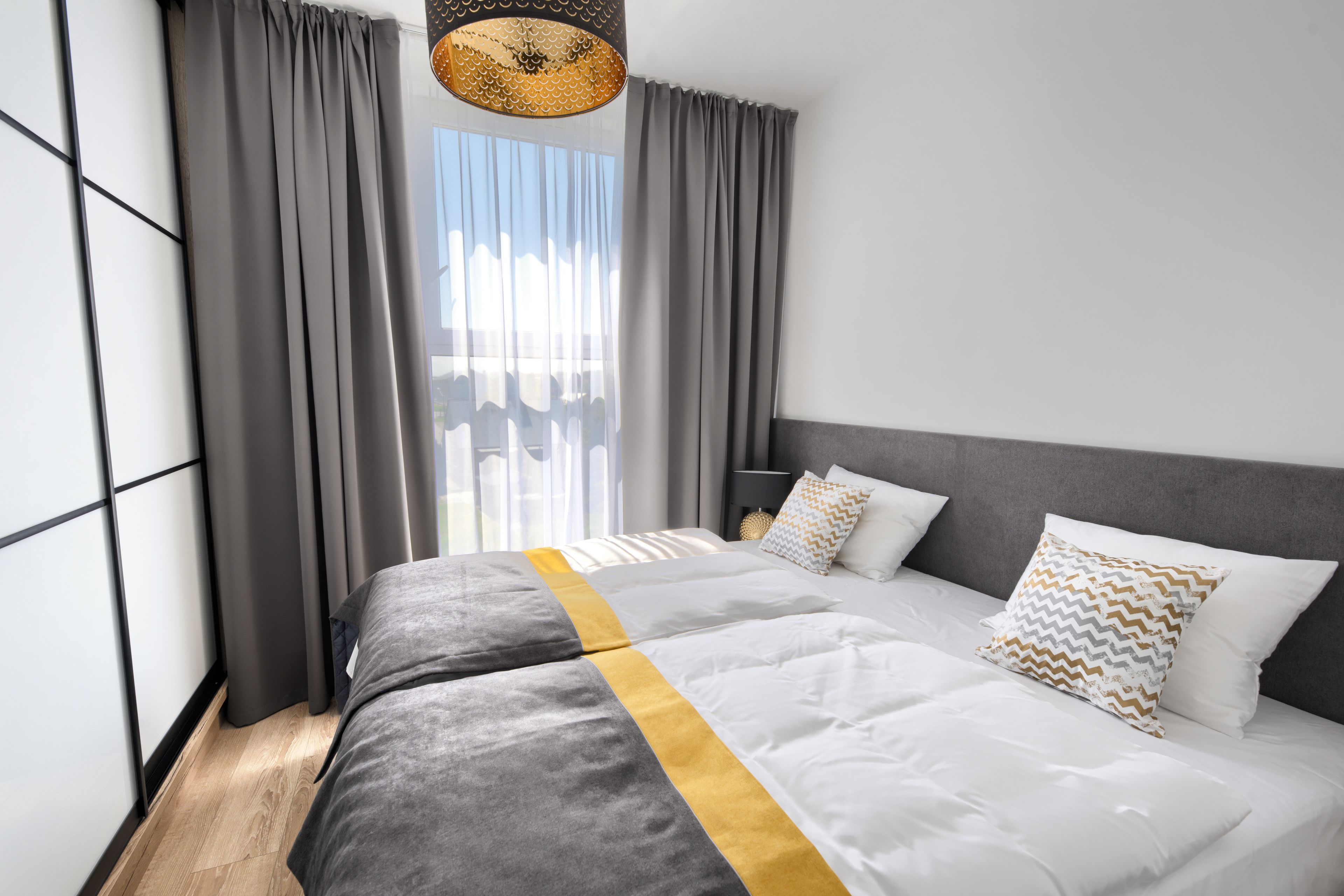A modern hotel room with a large bed, grey curtains, and a view of the city.
