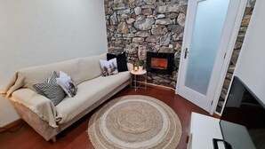 En hyggelig stue med en stenvæg, en beige sofa med stribede puder, en rund måtte og en pejs.