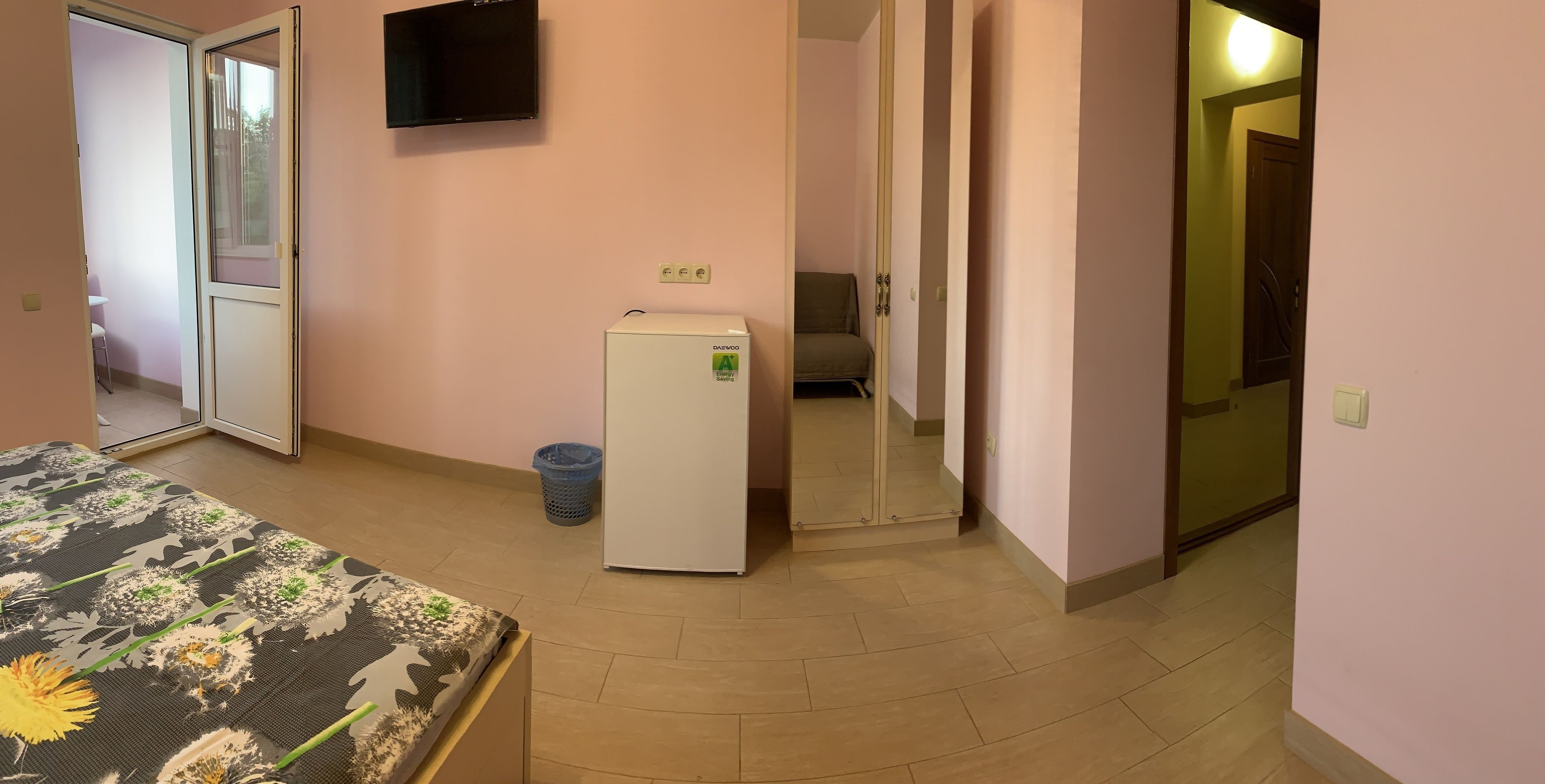 Quarto de hotel com cama, pequeno frigorífico, televisão e lixeira.