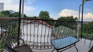 Un balcone con mobili in vimini, un tavolino in vetro e vista su un edificio e alberi.