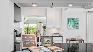 Une cuisine moderne avec des meubles blancs, un plan de travail noir et une vue sur la verdure à l’extérieur.