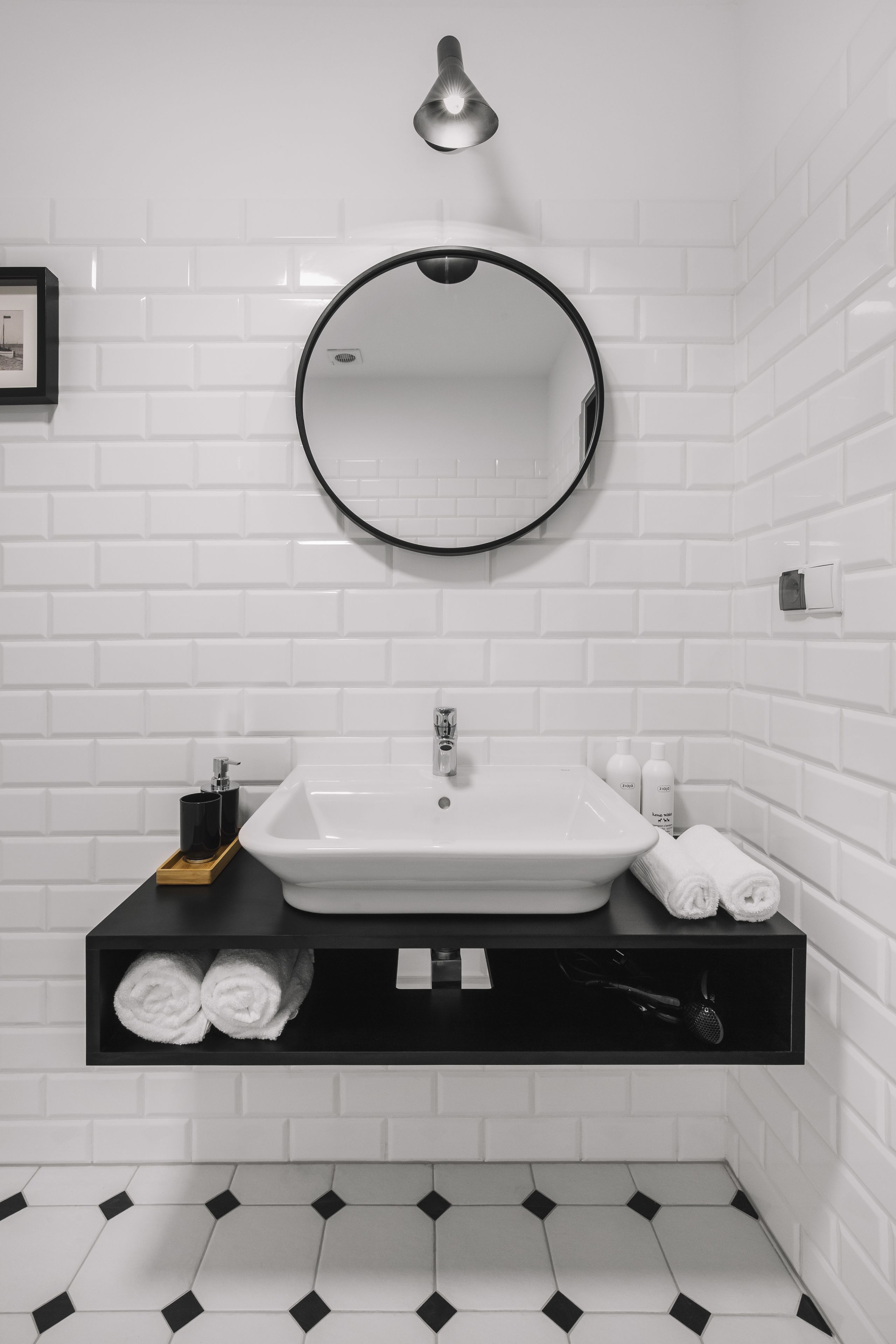 A bathroom with white subway tiles, a round mirror, a white sink, and a black vanity.