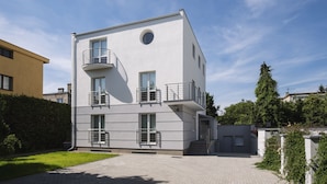 Un edificio moderno de varios pisos con balcones, un ventanal circular central y un área de entrada pavimentada.
