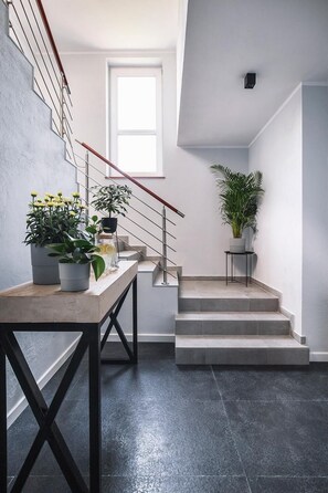 A modern staircase with a wooden handrail, a small table with potted plants, and a potted plant on a side table. - Villa Orla (Gdynia)
