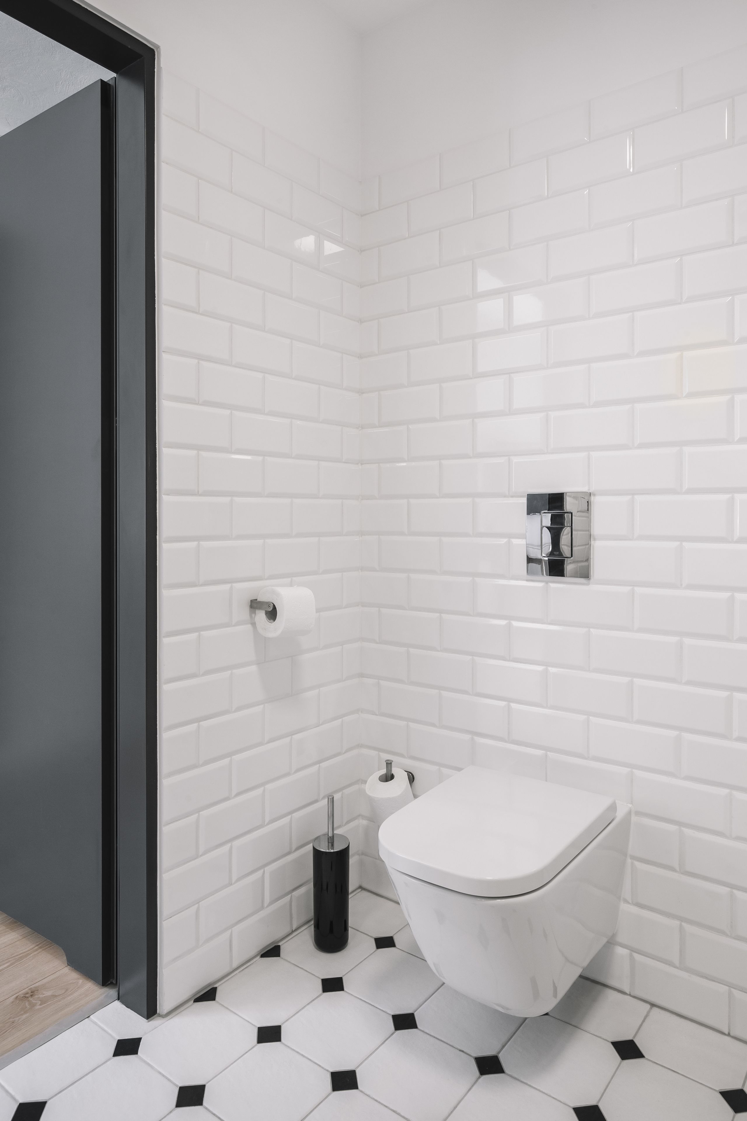 A bathroom with white subway tiles, a white toilet, and a black floor tile pattern.