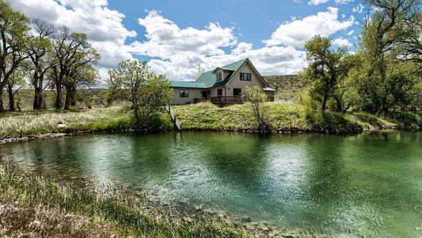 Una casa con techo verde, rodeada de árboles y un río.