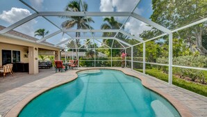 Une piscine dotée d’une structure en verre, entourée de mobilier d’extérieur et de palmiers.