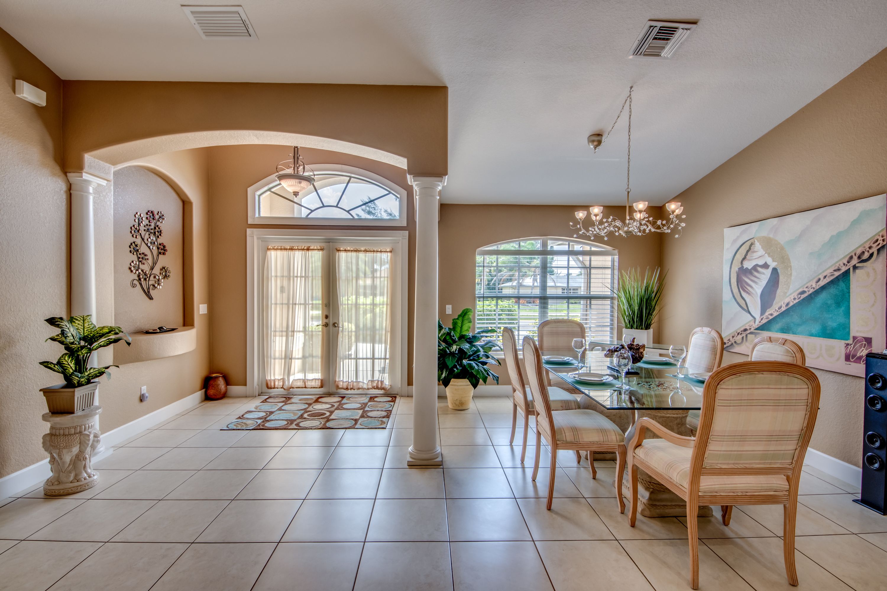 A spacious dining area with a glass table, cushioned chairs, and a chandelier.