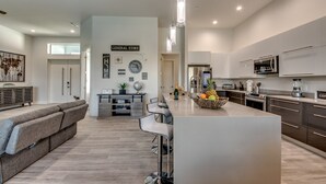 A modern kitchen with a central island, bar stools, and a dining area with a sofa and chairs. - Villa Southbreeze by Vacationhit (Cape Coral)