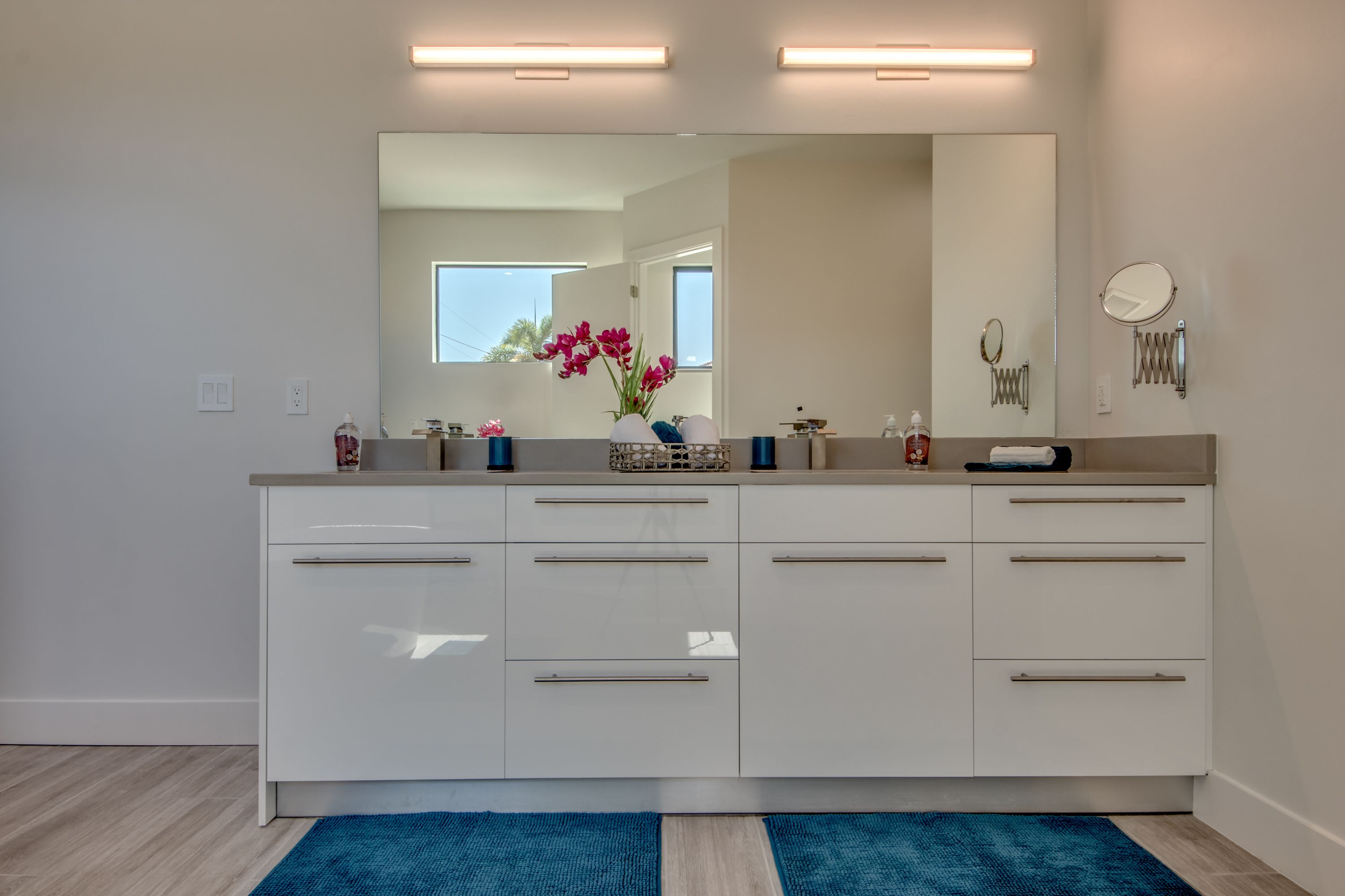 Un baño moderno con un espejo grande, muebles blancos y una alfombra azul.