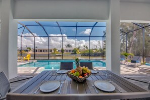 A dining area with a pool view, featuring a table with a fruit bowl, plates, and cutlery. - Villa Southbreeze by Vacationhit (Cape Coral)