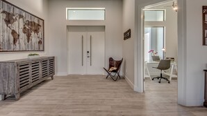 A spacious hallway with a wooden floor, a large world map on the left, a folding chair, and a desk with a laptop in the background. - Villa Southbreeze by Vacationhit (Cape Coral)