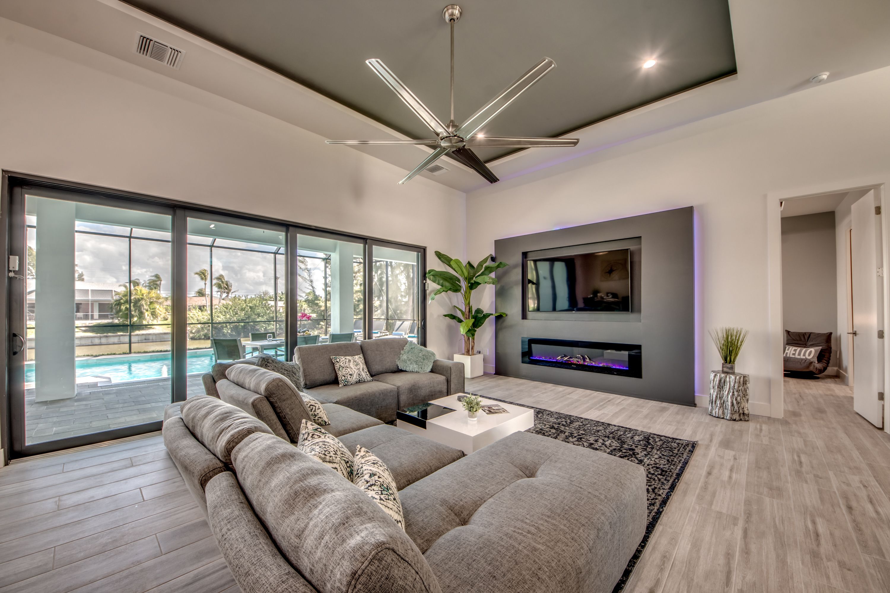 Uma sala de estar moderna com um sofá seccional grande, uma TV de tela plana na parede e um ventilador de teto.