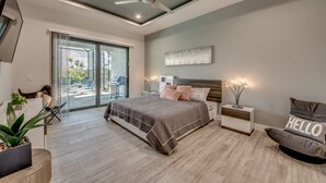A modern bedroom with a large bed, a ceiling fan, a bedside table with a lamp, and a view of the outdoors through a sliding door. - Villa Southbreeze by Vacationhit (Cape Coral)