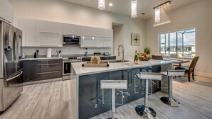 A modern kitchen with stainless steel appliances, a large island with bar stools, and pendant lighting. - Villa Southbreeze by Vacationhit (Cape Coral)