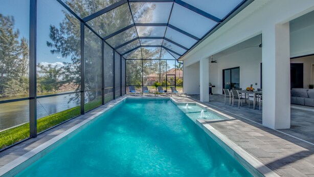 A covered swimming pool with clear views of a river and trees, surrounded by a modern patio area with outdoor furniture. - Villa Southbreeze by Vacationhit (Cape Coral)