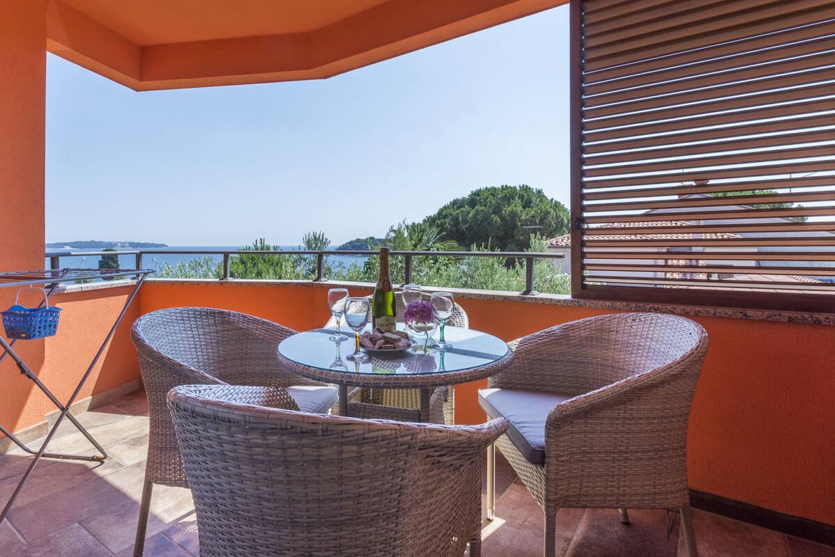 A balcony with wicker chairs, a glass table, and a bottle of wine.