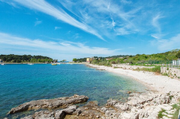 A coastal landscape with clear blue waters, rocky shorelines, and a distant view of buildings on a hill.
