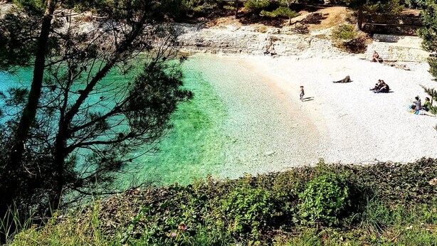Ein Strand mit klarem türkisblauem Wasser, umgeben von dichtem Grün und felsigem Gelände.