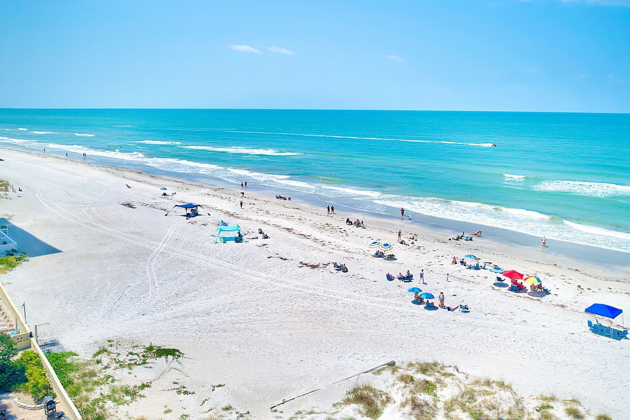 A beach with clear skies, a sandy shore, and a few umbrellas and beach chairs.