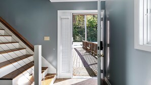 Una scala con gradini in legno e ringhiere bianche che conduce a una porta da cui si vede un pontile in legno e la vegetazione circostante.