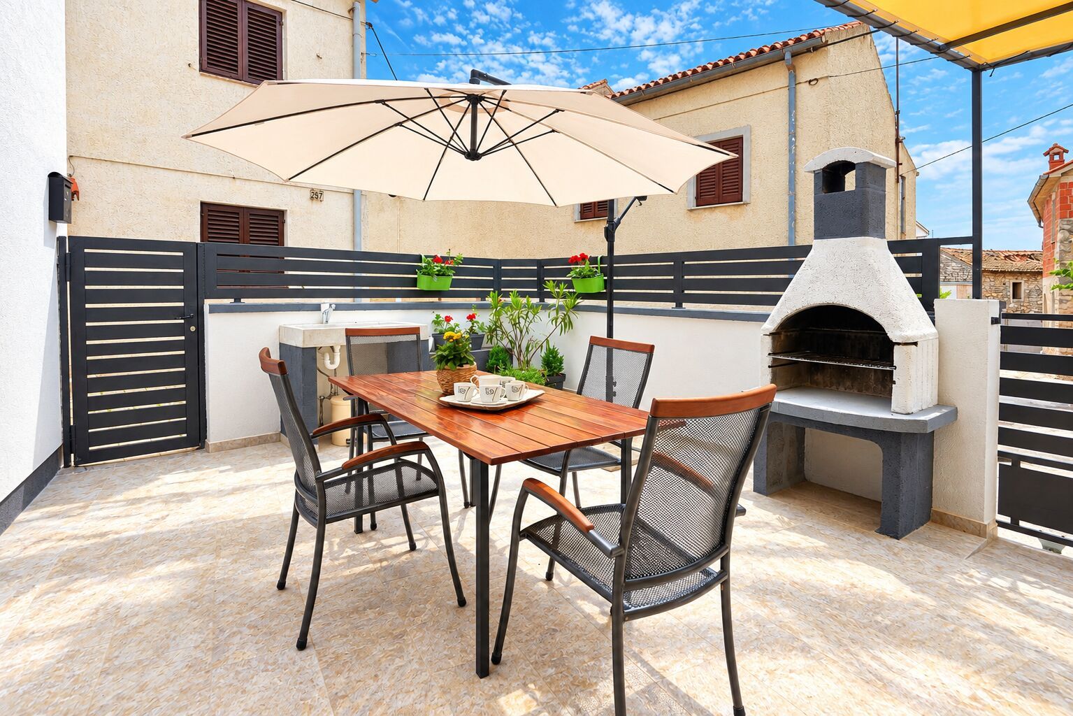 An outdoor patio with a table and chairs, a barbecue grill, and a potted plant.