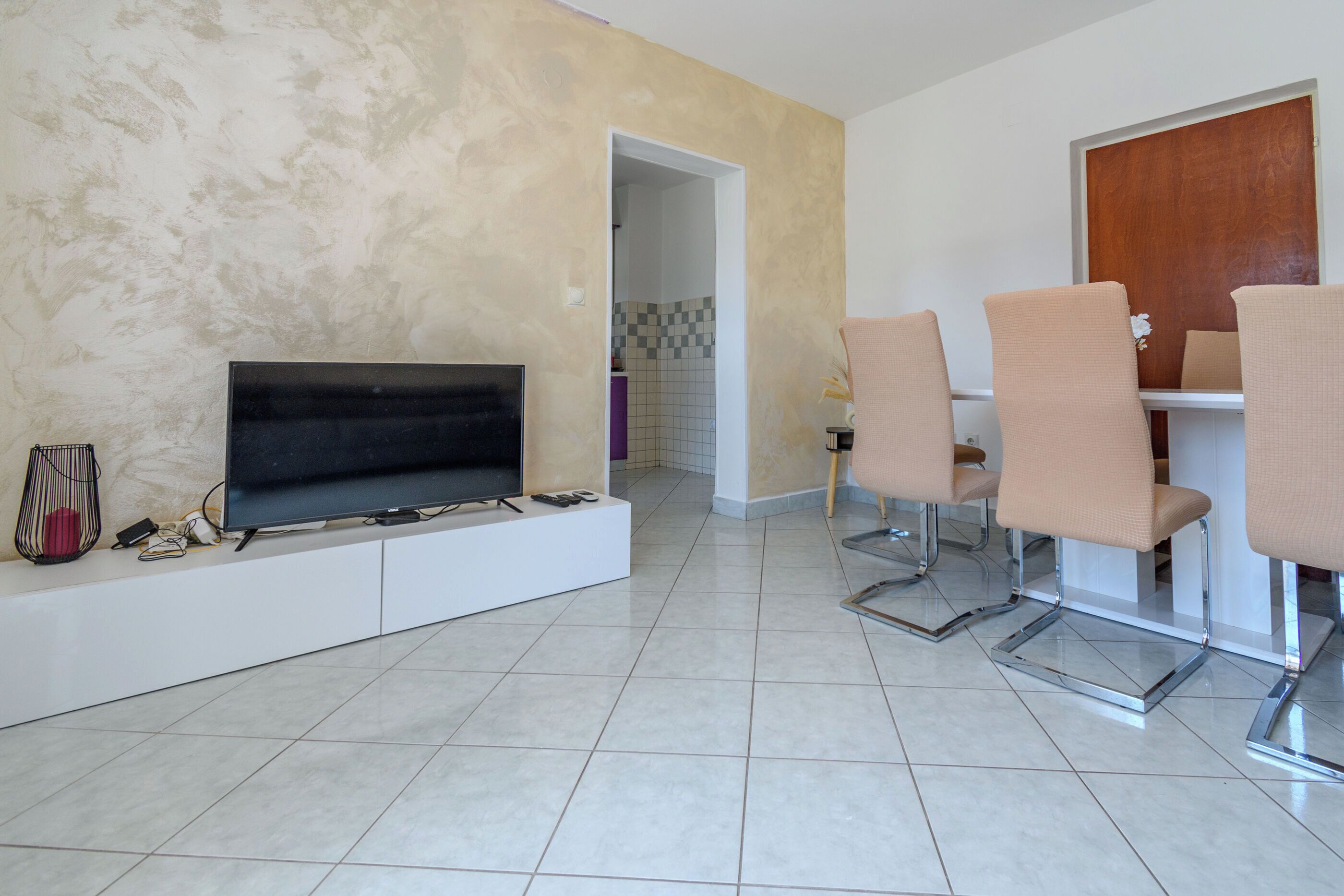 A modern living room with a flat-screen TV, a sofa, and a dining area with chairs.