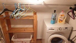 Ein Waschbereich mit Waschmaschine, einem Kleiderständer mit Wäsche und Waschmittelflaschen.