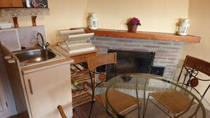 Eine kompakte Küche mit Spüle, kleinem Kühlschrank, Korbstühlen, einem Glastisch und einem Kamin.