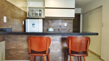 A kitchen with a wooden backsplash, a microwave, a refrigerator, and two wooden chairs.
