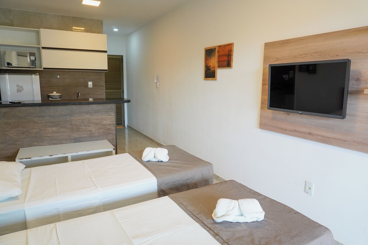 A hotel room with two beds, a TV mounted on the wall, a microwave, and a small kitchenette.
