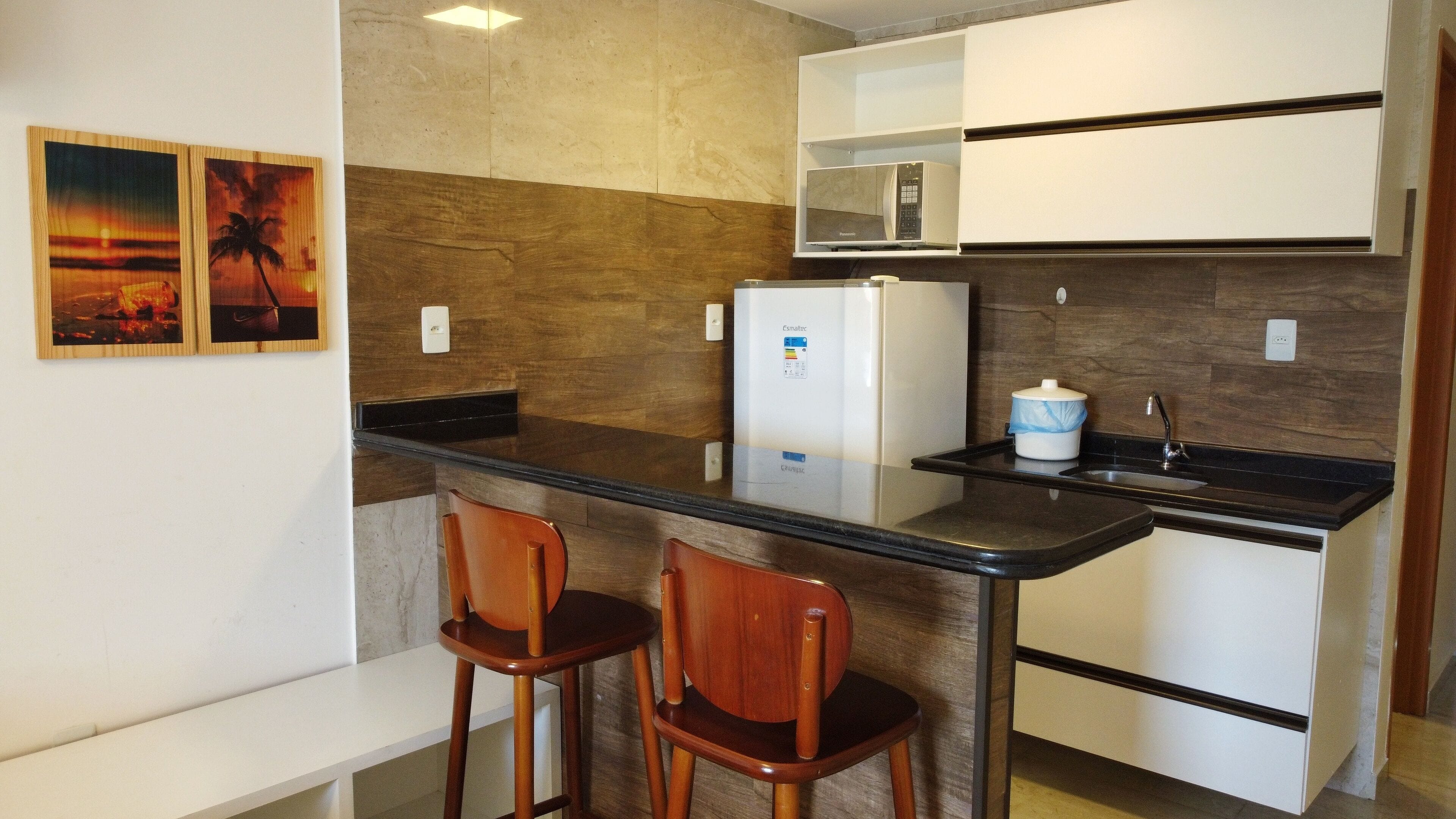 Cocina compacta con refrigerador, microondas y pileta. Hay dos sillas de madera y un banco.