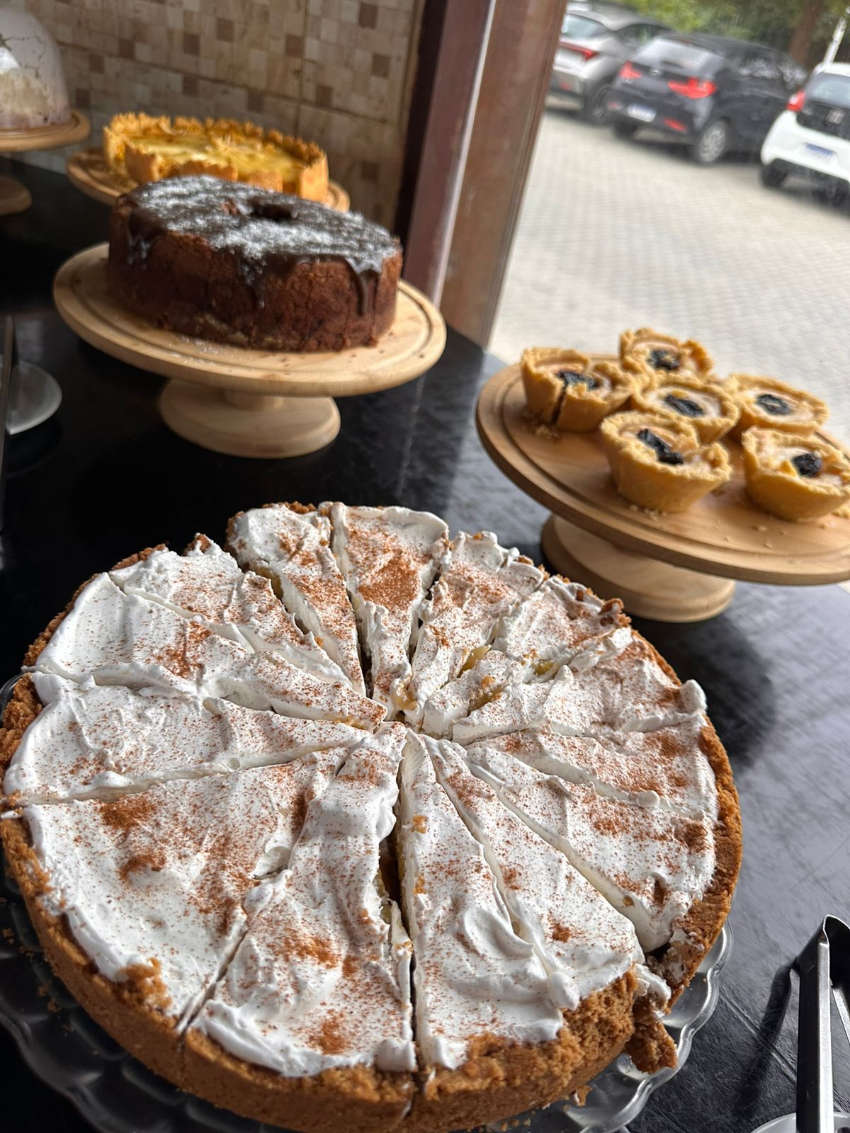 A dessert display with a pie, a cake, and tarts on wooden stands.