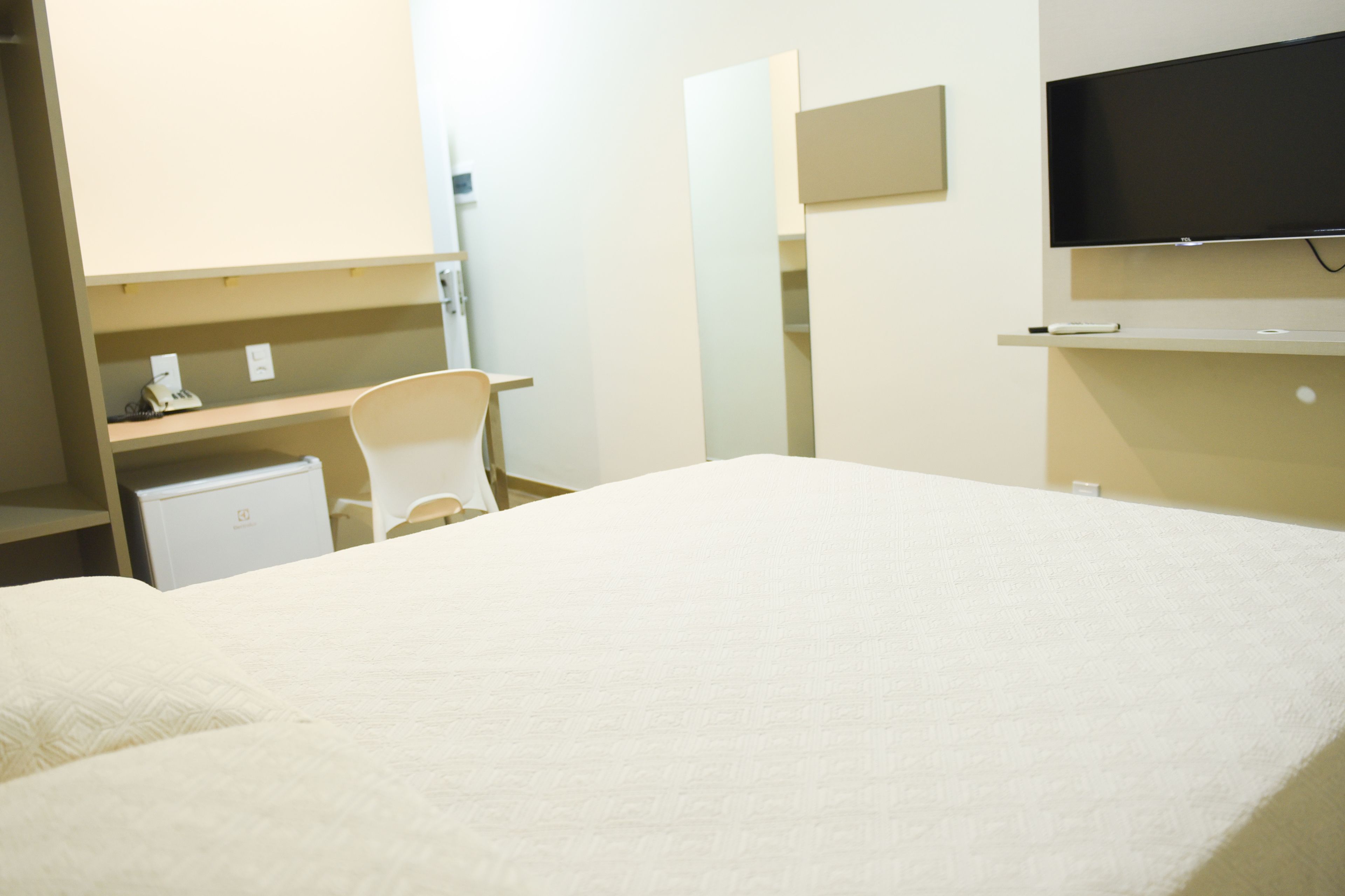 Una habitación de hotel con una cama, un escritorio, una silla, un televisor y un refrigerador pequeño.