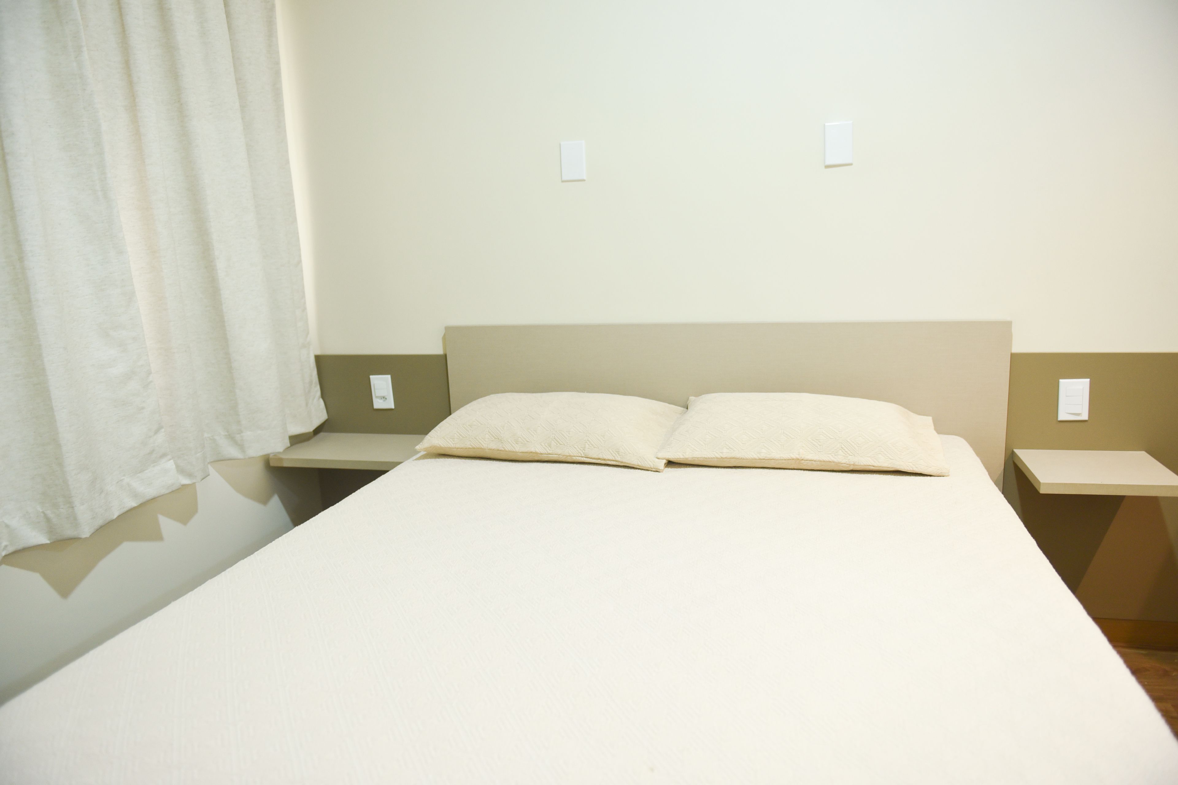A simple, clean hotel room with a single bed, two nightstands, and a plain wall.