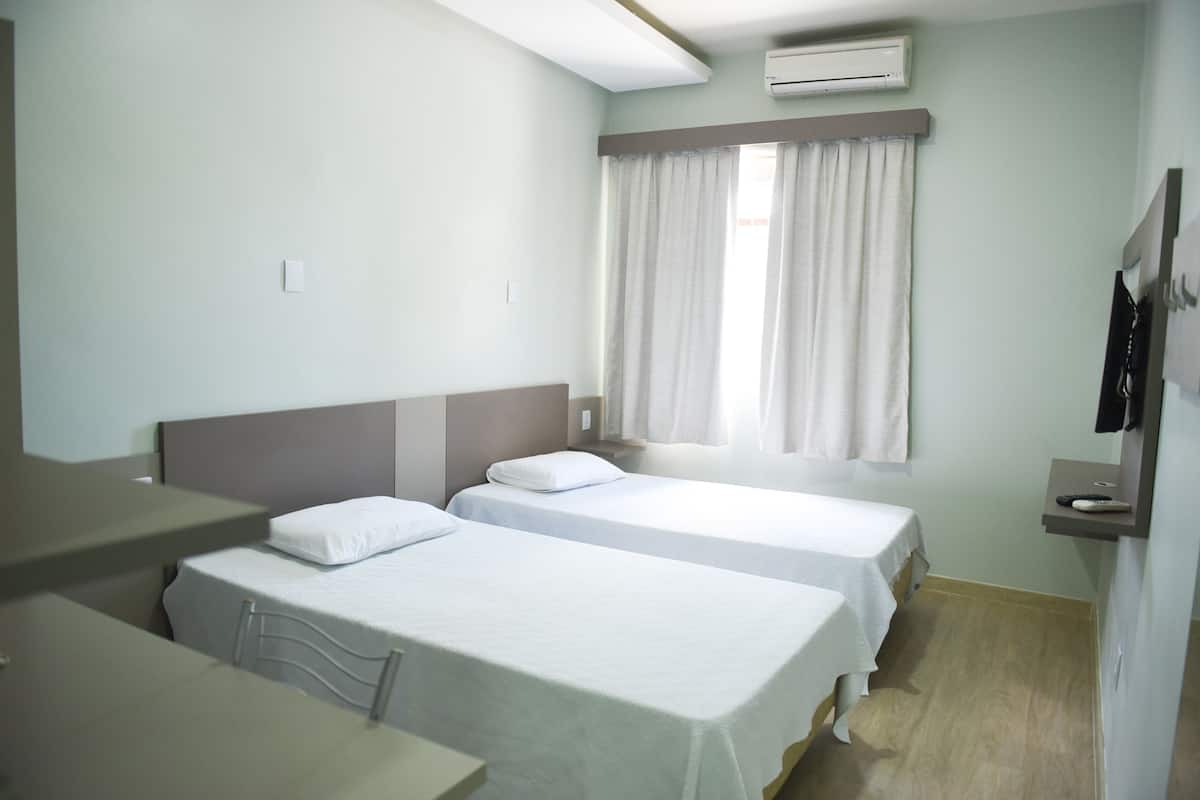A hotel room with two single beds, a desk, and a small table.