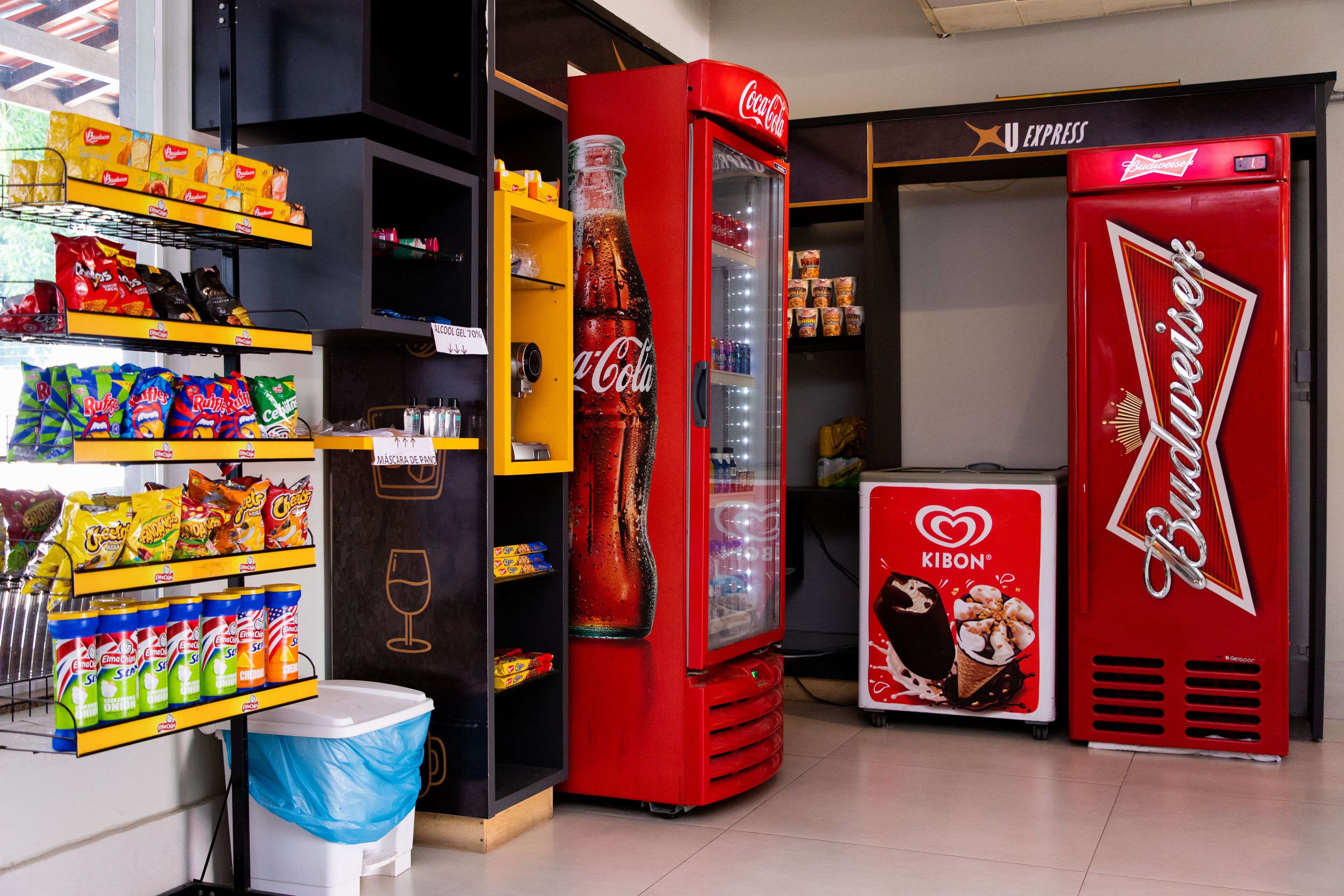 Zona de máquinas expendedoras con refrigeradores de Coca-Cola y Budweiser, y diversas opciones de bocadillos y bebidas.